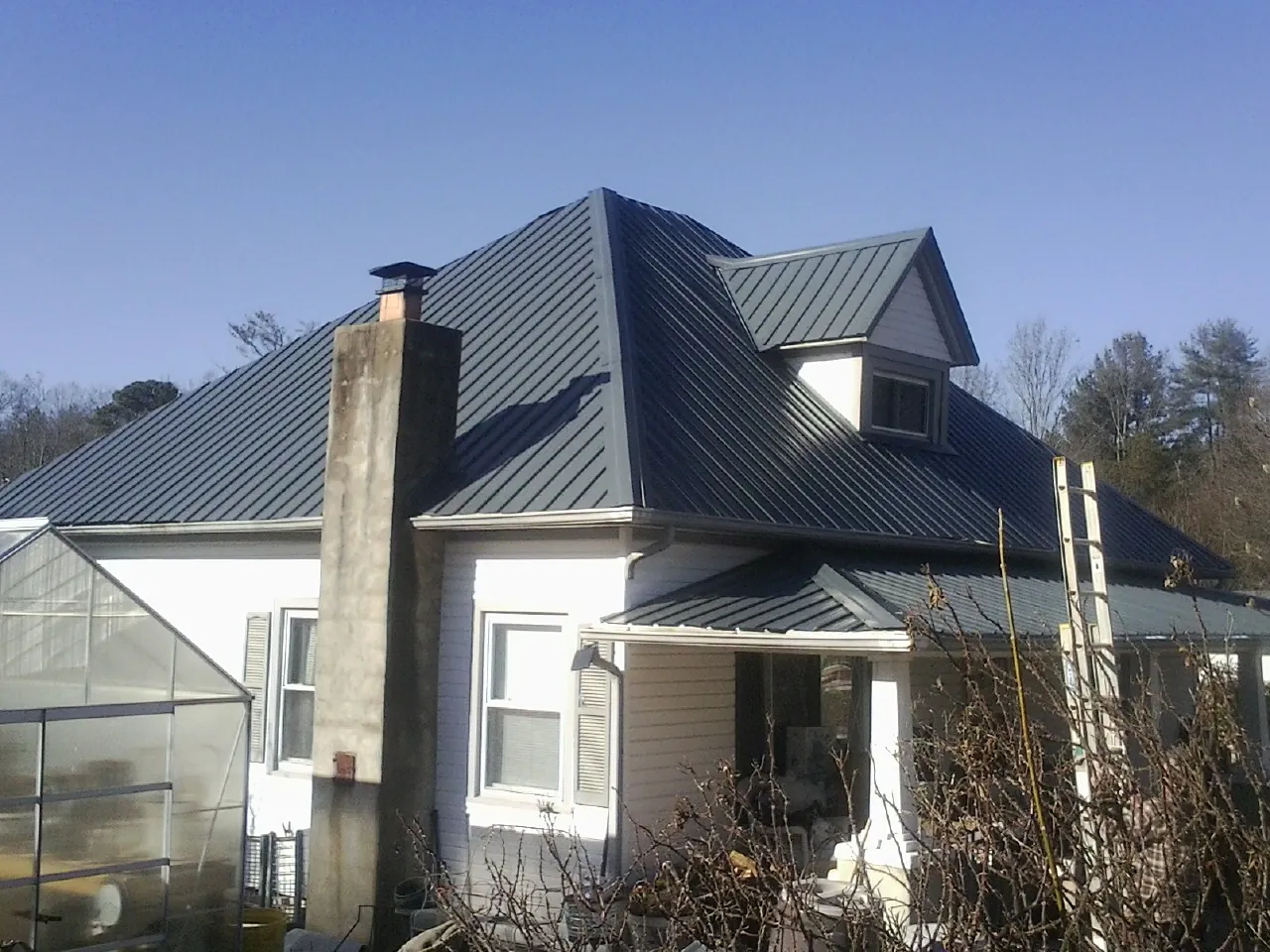 Dark blue standing seam metal roof on a white farmhouse with dormer — Slate & Tile Roof Repair by Roofing Brothers in Deansboro