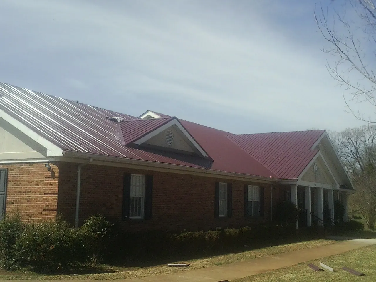Red metal roof with gabled entries on a long brick building, from a Hail Damage Roof Repair job in Deansboro