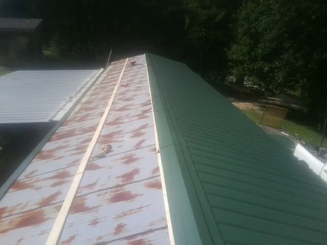 Old rusted panels beside newly installed green metal roofing — Wind Damage Roof Repair by Roofing Brothers in Deansboro