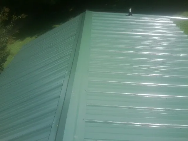 New green metal panels meeting at the ridge of a roof — Flat Roof Repair work by our crew in Deansboro