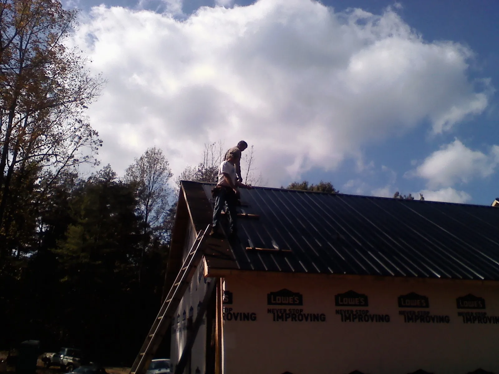 Roofer fastening dark metal panels high against a cloudy sky, from a Roof Inspection job in Deansboro