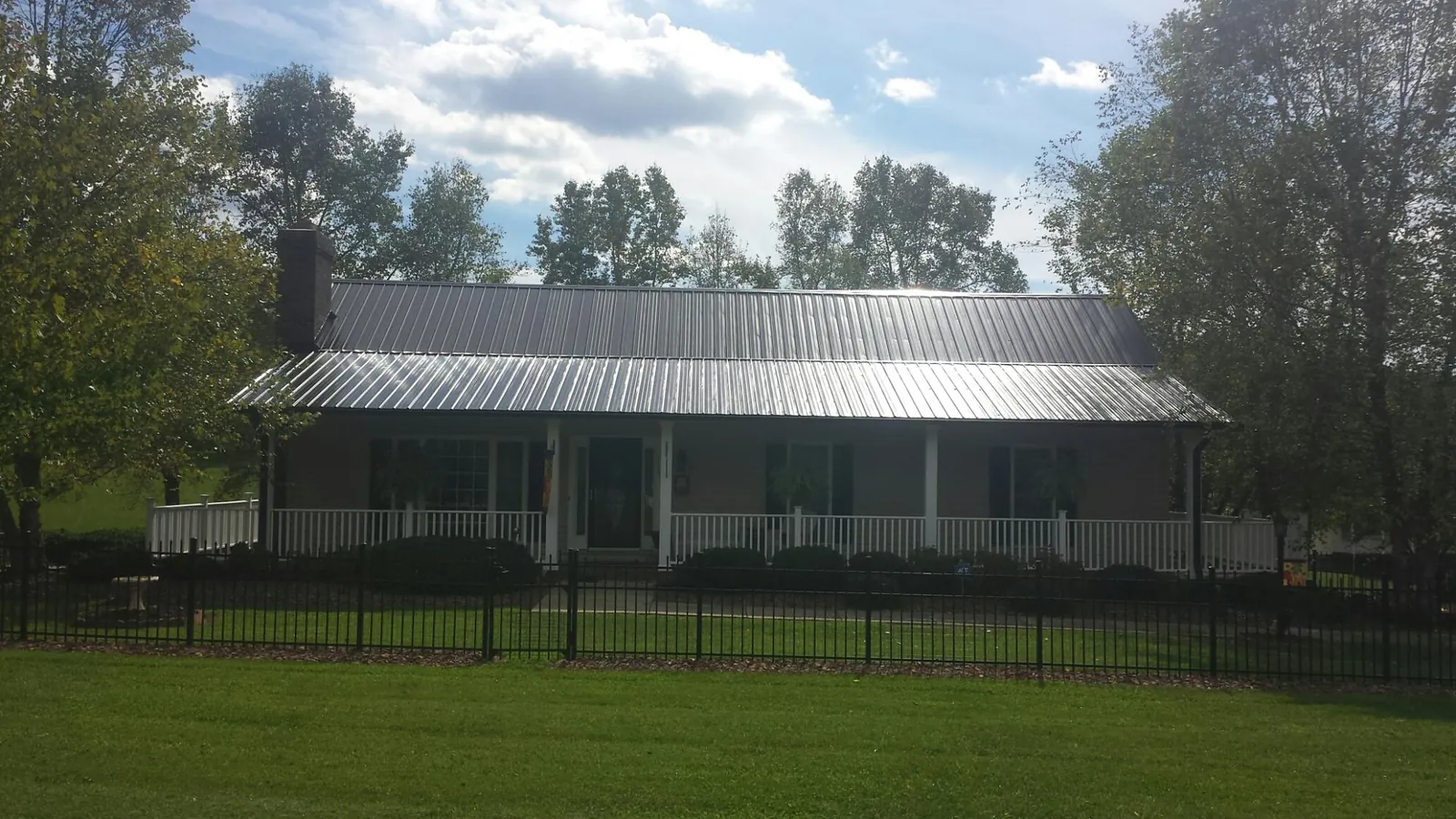 Gray metal roof on a brick ranch with a full width front porch — Gutter Guard Installation work by our crew in Deansboro