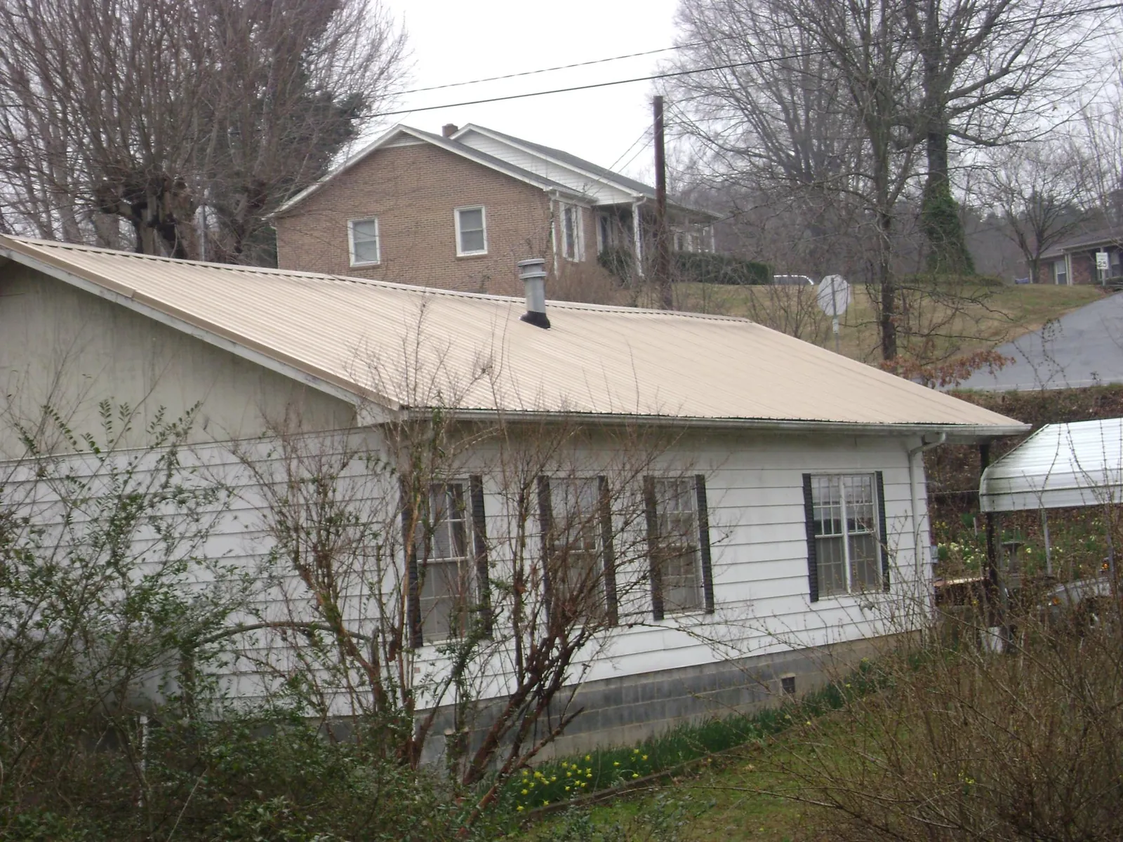 Tan metal roof on a white sided house set into a hillside — Commercial Roofing by Roofing Brothers in Deansboro