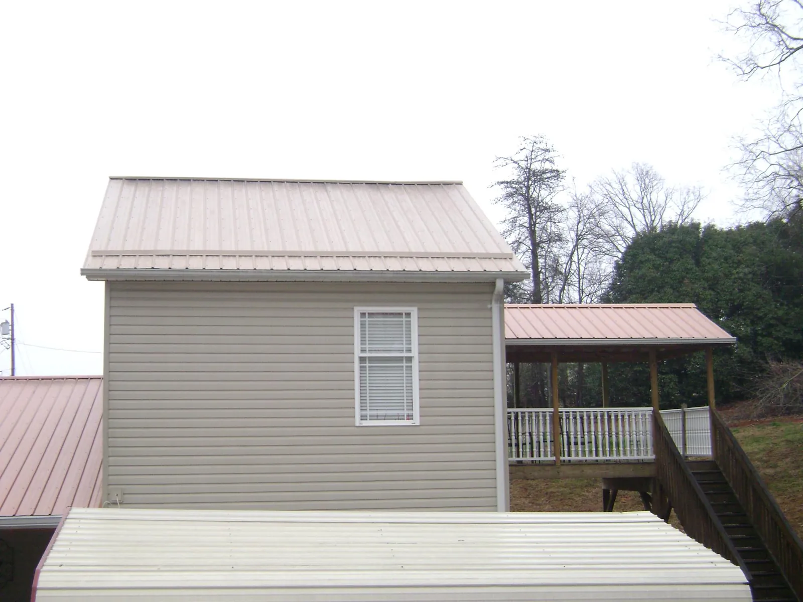 Tan metal roofs on a two story addition and attached porch, from a Roof Replacement job in Deansboro
